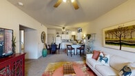This single-floor, 2-bedroom, 1-bathroom residence offers a thoughtfully designed open-concept layout that maximizes its living space. The combined living, dining, and kitchen area forms the heart of the home, highlighted by vaulted ceilings with a ceiling fan that enhance the sense of openness. The living room features neutral carpet, large windows that invite natural light, and direct sightlines to the outdoors. A kitchen peninsula with bar seating connects seamlessly to the dining and living areas, making it ideal for entertaining. The kitchen is equipped with white cabinetry extending to the ceiling, a full suite of white appliances including a refrigerator, electric range, microwave, and dishwasher, plus generous counter space and hardwood-style flooring. The dining area accommodates a round table and is accented by warm wood-tone flooring. Both bedrooms are carpeted and feature ceiling fans, ample closet space, and natural light from windows. The primary bedroom is generously proportioned, offering a comfortable retreat. The full bathroom includes a tub/shower combo with sliding glass doors, white cabinetry, and hardwood-style flooring. A hallway and closet complete the layout, adding practical storage solutions throughout this efficiently designed home.