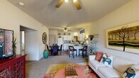 This single-floor, 2-bedroom, 1-bathroom residence offers a thoughtfully designed open-concept layout that maximizes its living space. The combined living, dining, and kitchen area forms the heart of the home, highlighted by vaulted ceilings with a ceiling fan that enhance the sense of openness. The living room features neutral carpet, large windows that invite natural light, and direct sightlines to the outdoors. A kitchen peninsula with bar seating connects seamlessly to the dining and living areas, making it ideal for entertaining. The kitchen is equipped with white cabinetry extending to the ceiling, a full suite of white appliances including a refrigerator, electric range, microwave, and dishwasher, plus generous counter space and hardwood-style flooring. The dining area accommodates a round table and is accented by warm wood-tone flooring. Both bedrooms are carpeted and feature ceiling fans, ample closet space, and natural light from windows. The primary bedroom is generously proportioned, offering a comfortable retreat. The full bathroom includes a tub/shower combo with sliding glass doors, white cabinetry, and hardwood-style flooring. A hallway and closet complete the layout, adding practical storage solutions throughout this efficiently designed home.
