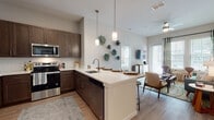 This single-floor residence offers a thoughtfully designed open-concept layout that seamlessly connects the kitchen, dining, and living areas. The kitchen is a standout feature, showcasing rich dark-brown cabinetry, a full suite of stainless steel appliances, white quartz countertops, a subway tile backsplash, and a large peninsula with bar seating—ideal for casual dining and entertaining. Light wood-style flooring runs throughout, complementing the neutral color palette and creating a warm, cohesive feel.

The living area benefits from generous natural light through multiple windows and is anchored by a ceiling fan overhead. Two well-proportioned bedrooms each feature large windows that invite in natural light and offer views of the surrounding exterior. One bedroom includes a distinctive sliding barn-style accent panel, adding a modern, functional touch.

The primary bathroom features a long vanity with dark wood cabinetry and a white countertop, providing ample storage. The secondary bathroom includes a full soaking tub and shower combination, finished with clean white subway tile. Both bathrooms continue the light wood-style flooring found throughout the residence. Overall, the space delivers a contemporary aesthetic with comfortable, functional design elements throughout.