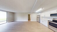 Located at 5903 Northwest 57th Court in Tamarac, Florida, this 2-bedroom, 2-bathroom single-floor home offers a clean, modern aesthetic throughout. The open-concept living and kitchen area forms the heart of the home, featuring light wood-look flooring, neutral warm-gray walls, and a textured ceiling. The kitchen is well-appointed with crisp white shaker cabinetry, white quartz countertops, a mosaic tile backsplash, and a full suite of stainless steel appliances including a refrigerator, range, microwave, and dishwasher. A dedicated closet provides additional storage off the kitchen area. The living area is generously proportioned and filled with natural light from a large sliding glass door that opens to an outdoor view, enhancing the sense of openness. Both bedrooms continue the light flooring and neutral palette, with the primary bedroom offering a comfortable footprint and direct closet access complete with built-in shelving and hanging rods. The two bathrooms are finished with white vanity cabinetry, white countertops, large mirrors, brushed nickel fixtures, and light wood-look flooring. One bathroom features a walk-in shower with built-in shelving. Hallways connect the rooms efficiently, contributing to a well-organized and functional floor plan throughout.