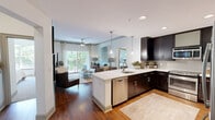 This well-appointed two-bedroom, two-bathroom residence on Carnegie Boulevard in Charlotte's sought-after SouthPark area offers a thoughtfully designed single-floor layout with contemporary finishes throughout. The open-concept kitchen and living area serves as the heart of the home, where rich dark-espresso cabinetry, white quartz countertops, a neutral tile backsplash, and a full suite of stainless steel appliances create a sleek, functional cooking space with hardwood flooring underfoot. The living room extends naturally toward a sliding glass door that opens onto a private balcony, flooding the space with natural light and offering peaceful views of mature tree canopies. The primary bedroom is generously proportioned, featuring plush carpeting, large windows with verdant outdoor views, a ceiling fan, and direct access to both a walk-in closet and a well-appointed en-suite bathroom. The primary bath showcases dark wood double vanities with white countertops, large-format tile flooring, and a tiled soaking tub and shower. The second bedroom is equally comfortable, and the second bathroom mirrors the refined aesthetic with marble-style tile and a clean white vanity. Two dedicated closets and two hallways provide excellent storage and circulation throughout the home.