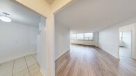 Located on the 18th floor at 185 Shaughnessy Blvd in Toronto's Don Mills neighbourhood, this one-bedroom, one-bathroom unit offers a well-organized layout with a generous overall footprint. Light wood flooring runs throughout the living areas and bedroom, creating a warm, cohesive aesthetic against the crisp white walls and trim.

The spacious living room is a standout feature, anchored by a wide bank of floor-to-ceiling windows that frame sweeping city skyline views and flood the space with natural light. A baseboard heating system runs along the window wall. The adjacent dining area is accented by an elegant chandelier and opens directly to the kitchen, which features white cabinetry, granite-style countertops, a double sink, and classic white tile backsplash, all set on light ceramic tile flooring.

The well-sized bedroom includes a large sliding-door closet and a bright window with additional city views, continuing the light and airy feel of the unit. The bathroom is finished with full white ceramic tile surround, a soaker tub with overhead shower, and clean, functional fixtures.

Connecting hallways provide a practical flow between all rooms, rounding out a thoughtfully arranged and bright urban residence.