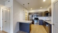 Located at 736 W State St in Farmington, Utah, this well-designed one-bedroom, one-bathroom unit offers a thoughtful layout across a single floor. The kitchen serves as a central highlight, featuring dark wood-grain cabinetry, a classic white subway tile backsplash, granite countertops, and a full suite of stainless steel appliances including a range, microwave, refrigerator, and dishwasher. A peninsula with pendant lighting overhead provides additional prep space and a casual dining option, while light wood-look flooring ties the area together. The bedroom is generously sized, finished with plush carpet, natural light from dual windows, and direct access to a walk-in closet, offering ample storage. The bathroom continues the modern aesthetic with a granite-topped vanity, wood-grain cabinetry, and a tub-shower combination, accented by a window for natural light. Additional practical features include a dedicated laundry area, a utility room with built-in shelving and an electrical panel, a hallway connecting the living spaces, and a private balcony. The unit's clean, neutral palette and contemporary finishes create a cohesive and functional living environment.