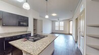 This single-floor unit is designed with an open, functional layout that seamlessly connects the kitchen and living areas. The kitchen serves as a central focal point, featuring dark espresso-toned cabinetry that extends to the ceiling, granite countertops, and a central island with an electric cooktop. Pendant lights hang above the island, providing focused task lighting, while the island's white base adds a clean contrast to the darker cabinetry. Black appliances, including a refrigerator, built-in microwave, and dishwasher, complete the kitchen's cohesive aesthetic. Wood-style flooring runs consistently throughout the unit, lending warmth and visual continuity to each room. The living area benefits from multiple windows fitted with blinds, allowing for adjustable natural light, and is finished with crown molding and a ceiling fan. The bedrooms are well-proportioned, with one featuring a tray ceiling, ceiling fan, recessed lighting, and natural light from multiple windows. Additional rooms offer wood-style flooring and ample wall space. The bathroom includes a tub-shower combination with a sliding glass door, a dark wall-mounted cabinet, and durable flooring. Built-in shelving and in-unit laundry connections add to the unit's practicality.