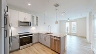 This well-appointed 1-bedroom, 1-bathroom unit offers a thoughtfully designed open-concept layout with contemporary finishes throughout. The kitchen and living area flow seamlessly together, anchored by a sleek peninsula with quartz countertops and pendant lighting. The kitchen is equipped with stainless steel appliances — including a refrigerator, range, microwave, and dishwasher — complemented by two-tone cabinetry featuring white upper cabinets with glass inserts and light gray lower cabinets, set against a clean white tile backsplash. Light wood-tone flooring runs throughout the unit, lending warmth and continuity to every room. The living area is bright and airy, with a ceiling fan and French doors that open to a private balcony with outdoor views. The bedroom is a comfortable size, featuring a ceiling fan, a large window with natural light, and direct access to a dedicated closet. The full bathroom is generously proportioned, showcasing a dual-sink vanity with dark countertops and black hardware, large-format tile flooring, a soaking tub, and a separate walk-in shower with tile surround. A dedicated closet with built-in shelving completes the unit, offering convenient storage. The overall ambiance is clean, modern, and move-in ready.