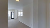 This single-floor, two-bedroom space offers a bright and functional layout designed with simplicity and comfort in mind. The interior is finished in crisp white walls throughout, creating a clean, neutral backdrop that feels open and versatile. Plush wall-to-wall carpeting in a warm beige tone runs through the main living areas, adding a soft, comfortable underfoot feel.

The layout flows naturally from the front entry, where a black-framed glass panel door allows natural light to filter in while providing a welcoming focal point. Moving deeper into the space, the living area transitions smoothly into a defined dining area, highlighted by a pendant light fixture that adds a subtle decorative touch overhead.

A window in the dining area draws in additional natural light, enhancing the airy, open feel of the space. Flush-mount ceiling lighting provides consistent illumination throughout. Clean white baseboards frame each room, contributing to the polished, well-maintained aesthetic. The overall ambiance is calm and move-in ready, offering a blank canvas well-suited for a variety of interior styles and furnishing arrangements.
