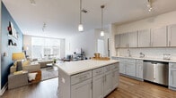 Located at 1–3 Maple St in Norwalk, CT, this well-appointed 2-bedroom, 2-bathroom residence offers a thoughtfully designed single-floor layout with modern finishes and a bright, welcoming ambiance. The open-concept kitchen and living area serves as the heart of the home, where warm wood-look flooring flows seamlessly underfoot. The kitchen is a standout feature, boasting gray shaker cabinetry, a classic white subway tile backsplash, quartz countertops, stainless steel appliances, and a large central island with pendant lighting — ideal for both cooking and entertaining. The adjoining living and dining area is anchored by a bold blue accent wall and oversized windows that flood the space with natural light and offer views of the surrounding neighborhood. The spacious primary bedroom features plush carpeting, large windows, and ample room to relax. The second bedroom is equally comfortable, with soft carpet and natural light. Both bathrooms are finished with gray vanities, white quartz countertops, and tub-shower combinations — one with wood-look tile flooring and the other with a subtle stone-patterned tile. Clean lines, neutral tones, and contemporary detailing give this residence a polished, modern character throughout.