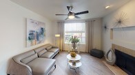This single-floor residence offers a thoughtfully designed layout that balances comfort and functionality. The kitchen is a standout feature, equipped with stainless steel appliances including a refrigerator, range, and microwave, complemented by granite-style countertops, white cabinetry, a double sink, and a breakfast bar peninsula that opens toward the living area. A pantry with built-in shelving provides ample storage. The living room is bright and welcoming, featuring wood-style flooring, a ceiling fan with light, and a large window dressed with floor-length curtains that allows generous natural light to fill the space. A glass sliding door connects the dining area to a covered outdoor patio, ideal for al fresco dining. The dining space is accented by a pendant light fixture overhead. The bedrooms feature plush carpet, ceiling fans, and warm neutral tones, offering a relaxing retreat. One bedroom includes a closet with sliding doors. The bathrooms are finished with white cabinetry, granite-style countertops, a tub-shower combination, and wood-style flooring. A hallway with decorative wall art connects the living and private spaces, adding a touch of personality throughout this clean and contemporary residence.