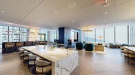 Located at 1909 Walnut Street in Philadelphia's vibrant Rittenhouse Square neighborhood, this single-floor amenity lounge is a masterclass in contemporary luxury design. The open-plan layout flows seamlessly across herringbone-patterned hardwood floors, connecting a series of distinct yet cohesive gathering spaces bathed in abundant natural light from expansive, floor-to-ceiling windows that frame striking views of the surrounding cityscape.

At the heart of the space sits a commanding marble-topped island bar, its dramatic white and gold veining set against a backdrop of teal-painted walls adorned with abstract gold brushstroke accents. Sleek white bar seating lines the island, while a fully stocked back bar with pendant lighting creates an inviting focal point. An adjacent lounge area features plush seating in rich jewel tones — deep teal, cognac, and warm grey — anchored beneath a statement brass chandelier and complemented by a bold blue tile fireplace surround.

Intimate seating alcoves positioned along the window line invite relaxed conversation, while a dedicated dining area with built-in bench seating and a long communal table offers a more structured gathering option. A powder room showcases artisan-level detail with bespoke teal and gold wallcovering and a marble vanity. French doors lead to an outdoor terrace, further enhancing the connection between interior elegance and the dynamic Philadelphia skyline.