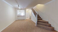 This two-story residence offers a practical and well-organized layout across two floors. The main level welcomes you through a secure entry door equipped with a deadbolt and chain lock, opening into a spacious carpeted living area bathed in warm, neutral tones. Track lighting overhead illuminates the open space, which flows seamlessly toward a pass-through kitchen. The kitchen features white cabinetry, tile backsplash, laminate countertops, and white appliances including a range, over-the-range microwave, and refrigerator. A convenient half bathroom on the main level includes a pedestal sink and tile flooring, ideal for guests.

A carpeted staircase with a white balustrade leads to the upper level, where both bedrooms are located. The primary bedroom is generously sized with tall ceilings, plush carpet, and a large window offering natural light and outdoor views. The second bedroom is equally well-proportioned with soft carpet and neutral walls. Each full bathroom on the upper level is finished with tile flooring, a tub-shower combination with tile surround, and a vanity with white cabinetry. Throughout, the space maintains a clean, neutral palette that provides a versatile and move-in-ready environment.