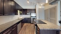 This well-appointed 2-bedroom, 2-bathroom single-floor unit offers a thoughtfully designed layout with consistent finishes throughout. The kitchen serves as a standout feature, showcasing dark espresso cabinetry extending to the ceiling, granite countertops, stainless steel appliances including a refrigerator, microwave, dishwasher, and range, as well as a double-basin sink and pendant lighting above the island. Wood-style flooring flows seamlessly through the kitchen and living areas, adding warmth and cohesion to the space. The living area is bright and open, featuring an exposed metallic duct, a ceiling fan, and glass French doors that invite natural light and outdoor views. Both bedrooms are generously sized with wood-style flooring and windows fitted with blinds. One bedroom connects directly to a bathroom via a hallway, offering added privacy. The bathrooms feature tile flooring, granite countertops, and functional vanities — one with dark navy cabinetry and the other with neutral tones. A walk-in closet with wire shelving is accessible from one of the bathrooms, providing ample storage. The unit's neutral color palette and modern finishes create a clean, contemporary ambiance throughout.