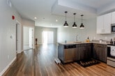 This single-floor residence at The Paseo Blvd in Kansas City, Missouri, showcases a thoughtfully designed open-concept layout with contemporary finishes throughout. Rich hardwood-style flooring flows seamlessly through the main living areas, creating a warm and cohesive aesthetic that connects the kitchen, dining, and living spaces.

The kitchen serves as a focal point of the space, featuring a peninsula with a two-toned design—dark lower cabinetry contrasted by crisp white upper cabinets. Granite countertops provide a durable and attractive work surface, while a full suite of stainless steel appliances, including a refrigerator, range, microwave, and dishwasher, supports everyday functionality. A trio of matte black pendant lights overhead adds a modern, industrial-inspired touch.

The open living area is generously proportioned, with recessed lighting and a sliding glass door fitted with vertical blinds that invites natural light and provides access to the outdoors. A separate bedroom features plush carpeting, a ceiling fan, and a tray ceiling detail that adds architectural interest.

The bathroom is finished with dark cabinetry, granite countertops, a large vanity mirror, light tile flooring, and a subway-tiled shower, combining practicality with a refined aesthetic.
