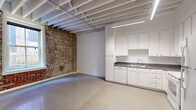 This studio in Memphis, TN offers a compelling blend of industrial character and functional design. The open-concept main living area immediately draws the eye with its striking exposed brick wall, which spans the full length of the space and adds rich texture and historic charm. Overhead, painted open-beam ceilings with visible structural joists reinforce the industrial aesthetic, while linear fluorescent lighting illuminates the polished concrete floors below.

The kitchen is thoughtfully laid out in an L-shaped configuration, featuring ample white cabinetry reaching toward the ceiling for generous storage, gray laminate countertops, and a full suite of white appliances including a refrigerator, range with overhead microwave, dishwasher, and double sink. The clean, bright cabinetry provides a crisp contrast to the rawer elements found throughout the space.

A window along the brick wall invites natural light and offers views of the surrounding urban streetscape, connecting the interior to the downtown Memphis environment.

The bathroom is well-appointed with a white vanity, gray countertop, and a glass-enclosed tiled shower featuring colorful mosaic tile accents in purple and teal tones, adding a distinct visual focal point. Together, these elements make this studio a distinctive urban retreat with standout architectural character.