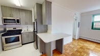 Located at 14 Marshall St in Irvington, NJ, this single-floor unit offers a thoughtfully updated interior with a clean, modern aesthetic throughout. The living area is bright and open, featuring warm parquet hardwood flooring that extends throughout the main spaces, crisp white walls, and a large window with green-framed trim that invites natural light and provides views of the surrounding neighborhood. A baseboard heating system runs along the base of the exterior wall, ensuring year-round comfort. The kitchen has been modernized with sleek gray wood-grain cabinetry, ample upper and lower storage, and stainless steel appliances including a gas range, microwave, and refrigerator. A white countertop peninsula extends into the living space, offering a convenient dining or workspace. The bedroom is generously proportioned with the same rich parquet flooring, bright white walls, and a closet with built-in storage. The bathroom has been elegantly finished with marble-look tile on both the floors and walls, a pedestal sink, a mirrored medicine cabinet, and a tub-shower combination enclosed with a sliding glass door, delivering a clean and polished feel. Overall, the unit presents a fresh and functional living environment with updated finishes throughout.