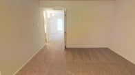 This two-floor residential space offers a straightforward and functional layout designed for comfortable everyday living. The interior is finished with wall-to-wall carpeting in a warm beige tone, providing a soft and cohesive feel across the living areas. Neutral cream-colored walls create a bright, airy atmosphere that makes each room feel open and welcoming.

The main living area flows naturally into adjacent spaces, connected by wide doorways that enhance the sense of openness and ease of movement throughout the floor plan. A ceiling fan is visible in the connecting room, offering both practical ventilation and a subtle decorative touch. Natural light filters in through a window at the end of the hallway, further brightening the interior.

The clean, uncluttered design of the space provides a versatile backdrop that can accommodate a variety of furnishing styles and personal touches. A thermostat is mounted on the wall, indicating climate control throughout the home. The two-floor layout offers added separation between living and private areas, providing functional zoning within the home. Overall, the space presents a tidy, move-in ready environment with a calm and neutral ambiance suited to a range of lifestyles.