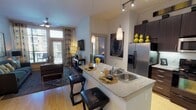 This 2-bedroom, 2-bathroom residence is thoughtfully designed with a contemporary open-concept layout that seamlessly connects the kitchen, dining, and living areas. The kitchen is a standout feature, showcasing rich dark cabinetry, granite countertops, a central island with bar seating, pendant lighting, stainless steel appliances including a French door refrigerator, a built-in microwave, and a tile backsplash with under-cabinet lighting. Light hardwood flooring flows throughout the main living areas, complementing the neutral color palette. The living room offers generous natural light through large windows dressed with patterned drapes, and features a wall-mounted flat-screen TV setup. Both bedrooms are carpeted and well-sized, with large windows providing outdoor views. The primary bathroom includes a wide vanity with dark cabinetry and granite countertops, a soaking tub with tiled surround, and tile flooring. The second bathroom mirrors this quality with similar finishes. Elevated ceilings add to the sense of openness throughout the space, while the overall design balances modern functionality with a warm, inviting ambiance.