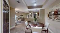 This single-story, 3-bedroom, 2-bathroom residence offers a thoughtfully designed open-concept floor plan that seamlessly connects the living, dining, and kitchen areas. The combined living and dining space features distinctive tray ceilings, neutral warm tones, and plush carpeting, creating an inviting and cohesive atmosphere. Large windows in the living room allow natural light to fill the space, complemented by a ceiling fan overhead. The kitchen is well-equipped with rich wood cabinetry, granite countertops, stainless steel appliances, tile flooring, track lighting, and a pass-through breakfast bar that opens directly to the dining area. The dining space itself benefits from its own tray ceiling detail, adding architectural character. The primary bedroom is a comfortable retreat featuring a ceiling fan, direct access to a closet, and an en-suite bathroom. The additional bedrooms are generously sized with carpeted floors and windows providing natural light. Both bathrooms are finished with granite countertops and warm wood vanities. A hallway connects the private sleeping quarters to the main living areas, rounding out a practical and comfortable floor plan.