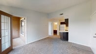 Located at 1704 Dublin Blvd in Colorado Springs, Colorado, this single-floor unit offers a practical and comfortable layout designed for everyday living. The living area is open and airy, finished with neutral-toned carpet and light gray walls that create a clean, understated atmosphere. A glass-paneled door leads directly to a private balcony, allowing natural light to filter into the space and providing an outdoor retreat.

The kitchen is positioned adjacent to the living area and features a peninsula-style island that serves as a natural divider between the two spaces. Dark espresso-toned cabinetry contrasts with light stone-look countertops, while wood-look vinyl flooring runs throughout the kitchen for easy maintenance. White appliances, including a refrigerator, dishwasher, stove, and microwave, are included. Ample upper and lower cabinet storage lines the walls, offering generous workspace.

The bedroom is well-sized, featuring plush carpet, multiple windows that bring in natural light, and a ceiling fan with integrated lighting. The bathroom includes a full tub and shower combination with white subway-style tile surround, wood-look flooring, dark cabinetry, and a marble-look countertop. The overall design maintains a consistent, neutral palette throughout.