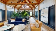 Located at 3 Woodview Way in Hopkinton, MA, this single-story clubhouse spans an expansive footprint designed to accommodate a variety of communal activities. The entrance greets visitors with soaring exposed timber-framed vaulted ceilings clad in warm wood, dramatic antler and chandelier lighting, and large-format tile flooring. Lush tropical plantings in deep navy planters add a vibrant, organic touch to the open-concept layout.

The main living area features the striking vaulted ceiling continuing overhead, with a built-in wet bar backed by bold blue tile, a large communal high-top table, and ample lounge seating arranged on geometric patterned rugs. A secondary living space offers a more intimate atmosphere, distinguished by richly detailed botanical wallpaper, round decorative mirrors, leather seating, and Edison bulb pendant lighting.

A dedicated game room showcases a classic black-and-white checkerboard tile floor, billiards and ping-pong tables, wainscoted blue walls, and garden views through multiple windows. The exercise room is well-equipped with cardio machines, strength equipment, herringbone hardwood-style flooring, a mounted TV, and a gingham-patterned accent wall, offering a bright and functional fitness environment.