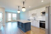 Located at 1140 Chambers Rd in Columbus, Ohio, this thoughtfully designed 1-bedroom, 2-bathroom residence offers a refined blend of modern finishes and functional living. The open-concept kitchen and living area serves as the heart of the home, anchored by a striking navy blue center island topped with granite countertops and illuminated by elegant globe pendant lights. White shaker cabinetry, a decorative tile backsplash, and a full suite of stainless steel appliances — including a French door refrigerator, microwave, and dishwasher — complete the chef-inspired kitchen. Light hardwood flooring flows throughout the main living areas, complementing the clean, neutral palette. A sliding door provides access to an outdoor balcony, allowing natural light to fill the space. The bedroom is a serene retreat featuring plush carpet, a paneled accent wall with wainscoting detail, and large windows with outdoor views. The en-suite bathroom showcases a marble-style tile floor, a white vanity with granite countertops, and an octagonal mirror with gold-tone fixtures. A spacious walk-in closet with multi-level shelving and hanging rods provides generous storage. A second full bathroom adds further convenience to this polished, move-in-ready residence.