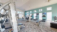 Located at 7755 Tierra del Sol Pkwy in Sparks, Nevada, this single-story fitness center is designed to support a comprehensive workout experience. The facility is divided into two distinct areas: a generously sized main gym floor and a bright, airy cycling studio.

The main gym area features a distinctive teal accent wall punctuated by a row of clerestory windows that flood the space with natural light. The patterned carpet flooring adds a modern aesthetic while providing comfort underfoot. This area is outfitted with a wide array of strength and cardio equipment, including treadmills, ellipticals, cable machines, selectorized weight machines, a multi-station functional trainer, free weights, and a plyo box for varied training routines. Mounted flat-screen televisions are positioned along the walls for entertainment during workouts.

The cycling studio offers a strikingly different atmosphere, featuring soaring vaulted ceilings, light hardwood flooring, and dramatic floor-to-ceiling windows that frame panoramic outdoor views of the surrounding Sparks landscape and distant hills. Multiple cycling bikes are arranged in the open space, which is bathed in natural light and serviced by a ceiling fan overhead. The minimalist, white-walled design of this room creates a clean, energizing environment ideal for focused training sessions.
