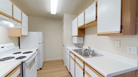 This single-floor residential unit offers a well-organized and functional layout with a clean, neutral aesthetic carried throughout. The galley-style kitchen is efficiently designed with white cabinetry trimmed in light wood, white appliances including an electric range, refrigerator, dishwasher, and built-in microwave, complemented by a stainless steel double sink and light wood-tone flooring. Ample upper and lower cabinetry provides generous storage space.

The open living area features warm laminate wood flooring, a textured ceiling, and a front entry door with a panel design, creating a welcoming and versatile space. A pendant light fixture anchors the dining or living zone, and sightlines extend toward a dedicated in-unit laundry area equipped with a full-size washer and dryer — a convenient and practical feature.

The bedroom is finished with plush wall-to-wall carpeting, a window with horizontal blinds for natural light and privacy, and access to a spacious walk-in closet outfitted with wire shelving and hanging rods.

The bathroom is clean and functional, featuring a full-size tub and shower combo, a single-sink vanity with white countertops and wood-accented cabinetry, a large mirror with overhead lighting, and durable wood-tone flooring. Textured ceilings appear consistently throughout, adding a subtle design detail to the overall space.