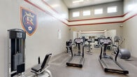 This community facility is thoughtfully organized across a single floor, offering a comprehensive fitness and gathering experience. The two entrance lobbies set a welcoming tone, featuring light-toned ceramic tile flooring, skylights that flood the space with natural light, and built-in mailbox banks lining the walls — a practical amenity for residents. Glass double doors provide easy access and contribute to an open, airy feel throughout.

The facility houses two distinct exercise rooms catering to a range of fitness needs. The first is a spacious, high-ceilinged gym adorned with team spirit décor, including Real Salt Lake and University of Utah logos. Red accent stripes run along the upper walls, and a row of clerestory windows allows ample natural light. This room is equipped with treadmills, cable weight machines, leg press equipment, and elliptical trainers, with large mirrors enhancing the sense of space.

The second exercise room offers a more intimate setting, featuring patterned teal and grey carpet, recessed lighting, and windows overlooking the exterior. It includes ellipticals, a stationary bike, and exercise balls with accessories for functional training.

The lounge areas provide a comfortable retreat, with carpeted flooring, wall-mounted work counters, bar-style seating, and decorative wall art, making them ideal for casual socializing or individual use.