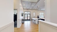 Located at 20 Parsippany Rd in Whippany, NJ, this amenity suite offers a thoughtfully designed, multi-functional space spread across a single floor. The layout comprises three distinct areas, each serving a specific purpose while maintaining a cohesive, contemporary aesthetic throughout.

The central lounge and social area is the heart of the space, featuring warm hardwood flooring, elevated coffered ceilings with recessed lighting, and large double-pane entry doors that flood the interior with natural light. A long white quartz countertop island with bar-height seating anchors the room, complemented by a navy blue tufted Chesterfield sofa, rounded cream accent chairs, and wood-framed seating arranged around a central coffee table. A wall-mounted flat-screen TV, a classic arcade game, and a built-in wet bar with navy cabinetry add both functional and entertainment value to the area.

The fitness center is a dedicated workout space outfitted with a full lineup of cardio equipment, including ellipticals, stationary bikes, and additional machines. Durable flooring, linear LED ceiling lighting, wall-mounted TVs, and a full rack of free weights ensure a comprehensive exercise experience. Natural light filters in through multiple windows with blinds.

Completing the suite are the restroom facilities, finished with large-format tile walls, slate-toned floor tiles, and sleek dark matte partition stalls, delivering a clean and modern aesthetic.