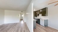 Located at 3070 W Del Monte Dr in Anaheim, CA, this single-story, one-bedroom, one-bathroom residence offers a practical and well-organized layout across a comfortable footprint. Light-toned, wood-style plank flooring runs consistently throughout the space, lending a cohesive and clean aesthetic from room to room.

The living room serves as the central gathering area, featuring a large window that invites natural light and an in-wall air conditioning unit. A hallway connects the living area to the rest of the home, with two closets providing ample storage along the way.

The galley-style kitchen is efficiently designed with dual runs of cabinetry featuring dark, glossy cabinet fronts contrasted against white countertops. White appliances include a gas range, over-the-range microwave, dishwasher, and a single-basin sink—offering full functionality in a compact format.

The spacious primary bedroom includes a window with exterior views, a textured ceiling, and direct access to a vanity area with a large mirror and wall-mounted lighting. An adjoining full bathroom features a combined tub and shower with clean white surround and chrome fixtures.

Textured ceilings are present throughout, and the neutral white walls provide a versatile backdrop throughout this well-maintained Anaheim residence.