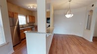 This well-appointed 2-bedroom, 2-bathroom single-story home offers a thoughtfully designed open-concept layout that promotes a seamless flow between living spaces. The kitchen is equipped with warm honey-toned wood cabinetry, granite countertops, a stainless steel dishwasher, and a built-in oven. A peninsula with a granite overhang provides convenient bar-style seating and serves as a natural divider between the kitchen and the adjoining living area. Hardwood-style flooring runs throughout the main living spaces, adding warmth and continuity to the design. The living area is bright and open, enhanced by a stylish geometric pendant light fixture that anchors the space. A window in the kitchen allows natural light to fill the area, contributing to the home's airy and welcoming ambiance. The clean white walls and neutral palette provide a versatile backdrop suitable for a variety of interior styles. The single-floor layout ensures easy accessibility and a cohesive living experience throughout. This home combines functional design with comfortable finishes, making it an ideal space for everyday living.