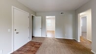 This single-floor unit offers three bedrooms, one bathroom, a kitchen, a hallway, and four closets within a practical, efficiently organized layout. Neutral gray walls and a mix of carpet and hardwood-style flooring run throughout, creating a cohesive aesthetic. The spacious primary bedroom features two closets—including a walk-in—carpet flooring, and access to an adjoining room with a window providing natural light. The two additional bedrooms are carpeted and each equipped with a ceiling fan and window overlooking greenery, offering a bright and comfortable atmosphere. Each secondary bedroom also includes a sliding or standard closet for storage. The kitchen is outfitted with white cabinetry, granite-style countertops, a gas range, dishwasher, refrigerator, and a stainless steel sink, complemented by hardwood-style flooring and a window. The bathroom features white subway tile walling, a bathtub-shower combination, and wood-look tile flooring. A sliding glass door in the living area opens to an outdoor balcony, adding a notable connection to the exterior.