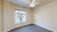 Located at 1129 SW Washington St in Portland, Oregon, this 2-bedroom, 1-bathroom unit offers a practical and efficiently designed single-floor layout. The entry hallway, accented by a bold blue front door and carpeted flooring, provides a welcoming passage into the space. Warm beige walls and gray carpet carry throughout the unit, creating a cohesive and neutral aesthetic.

The primary bedroom is the most spacious room in the unit, featuring a ceiling fan with light fixture, a baseboard heating unit, and a window that frames views of the surrounding urban streetscape, allowing natural light to fill the room. The second bedroom mirrors this layout with its own ceiling fan and window overlooking the cityscape.

The kitchen is compact and functional, equipped with warm wood-toned cabinetry, a dark countertop, and a white refrigerator. It opens to a carpeted living or dining area, maximizing the usable footprint of the space.

The bathroom is clean and straightforward, featuring a single-sink vanity with wood cabinetry and a dark countertop, a toilet, and a walk-in shower with chrome fixtures and grab bars. Light tile flooring and a ventilation unit complete the room. The unit's efficient design makes it a practical option for those seeking a manageable footprint in a central Portland location.
