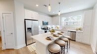 This 960-square-foot single-floor apartment offers a thoughtfully designed layout with 2 bedrooms, 2 bathrooms, a combined kitchen and living area, a dedicated laundry room, and a closet. Light wood-tone flooring runs throughout, creating a cohesive, airy aesthetic.

The open-concept kitchen is a standout feature, equipped with white shaker cabinetry, white quartz countertops, a subway tile backsplash, and a full suite of stainless steel appliances including a refrigerator, range, microwave, and dishwasher. A central island with pendant lighting provides seating for up to four and doubles as additional prep space.

The living room receives ample natural light through multiple windows fitted with blinds and sheer drapes, and includes a ceiling fan overhead. Both bedrooms continue this bright, open feel, each featuring ceiling fans, natural light, and access to closet space.

The two bathrooms are finished with white cabinetry, quartz countertops, and illuminated mirrors. The primary bathroom features an elongated vanity layout for added functionality. The in-unit laundry room accommodates a full-size side-by-side washer and dryer with built-in shelving above for storage. The unit combines modern design with practical amenities throughout.