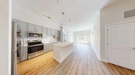 This well-designed single-floor residence offers three bedrooms and two bathrooms within a thoughtfully laid-out floor plan. The open-concept kitchen and living area serves as the heart of the home, featuring a central island with a clean white countertop, gray shaker-style cabinetry extending to the upper walls, and a full suite of stainless steel appliances including a range, microwave, and refrigerator. Pendant lighting above the island adds a modern touch, while track lighting illuminates the kitchen workspace. Light-toned hardwood flooring flows seamlessly throughout the entire home, creating a cohesive and airy feel. The living area extends naturally from the kitchen, benefiting from a large window that invites an abundance of natural light. Each of the three bedrooms is finished with the same warm hardwood flooring and neutral wall tones, providing versatile, move-in-ready spaces. The bedrooms feature windows with blinds that allow for ample natural light and outdoor views. The primary bedroom offers a generously sized layout. Clean white walls and consistent finishes throughout give the home a bright, modern aesthetic that is both functional and welcoming.