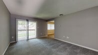 This single-floor unit offers a practical and comfortable layout with a consistent design language throughout. The living room is generously proportioned, featuring plush wall-to-wall carpeting in a neutral gray tone, textured ceilings, and a sliding glass door fitted with vertical blinds that opens onto a private balcony with outdoor views of surrounding greenery — a notable source of natural light.

Adjacent to the living area, the kitchen is well-equipped with warm-toned wood cabinetry, dark granite-style countertops, and a full suite of black appliances including a refrigerator, gas range, built-in microwave, and dishwasher. Light wood-look vinyl flooring ties the kitchen together cleanly.

The bedrooms continue the neutral carpet and gray wall palette, offering comfortable proportions. One bedroom features a double-door closet, while another includes an open closet alcove and windows with blinds for natural light. The bathroom presents a clean, functional design with wood-look vinyl flooring, a white vanity with cabinet storage, and a full tub-shower combo with built-in shelving and a curved curtain rod.

Overall, the unit maintains a cohesive, move-in-ready aesthetic with neutral tones throughout.