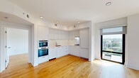 This thoughtfully designed 2-bedroom, 2-bathroom residence offers a clean, contemporary aesthetic throughout its single-floor layout. Wide-plank hardwood flooring flows seamlessly through every room, complemented by crisp white walls and recessed lighting that create a bright, airy atmosphere.

The open-concept kitchen, dining, and living area serves as the heart of the home. The chef's kitchen is outfitted with sleek, handle-front white cabinetry extending to the ceiling, a striking marble-look backsplash and countertops, a stainless steel undermount sink, a gas cooktop, and a double wall oven — delivering both style and functionality. The living area is bathed in natural light from floor-to-ceiling black-framed windows that frame expansive views of the surrounding cityscape and tree canopy.

The primary bedroom is a well-proportioned retreat featuring large windows with scenic outdoor views and roller shades for privacy. The second bedroom is equally light-filled with direct access to outdoor views. Three hallways connect the living spaces efficiently, each with built-in closets providing ample storage.

Both bathrooms are finished with large-format neutral tile, white cabinetry with marble-look countertops, undermount sinks, and chrome hardware. The full bath features a soaking tub with a tiled surround. The overall design is cohesive, modern, and move-in ready.