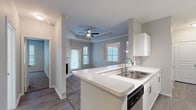 This single-story residence presents a cohesive, modern design throughout its open-concept layout. The kitchen is well-appointed with white cabinetry, light stone countertops, gray subway tile backsplash, stainless steel appliances, and wood-look flooring. A peninsula with a double sink connects the kitchen to the living and dining areas, creating a functional flow between spaces.

The living room serves as a central highlight, featuring a tray ceiling with crown molding, a ceiling fan, a corner fireplace with a white mantel, and a door providing access to the exterior. Natural light enters through multiple windows fitted with blinds throughout the unit.

The bedrooms are carpeted and generously sized, each equipped with ceiling fans and windows that bring in ample natural light. One bedroom includes direct access to a full bathroom, which features a tub-shower combination, white vanity with stone countertops, and wood-look flooring. An additional bathroom mirrors this clean aesthetic with matching finishes.

The interior palette of soft gray walls, white trim, and consistent flooring choices throughout creates a unified, neutral ambiance well-suited for a variety of furnishing styles.