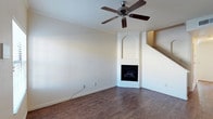 This two-story home combines classic architectural details with a practical and welcoming layout. The main living area sets a warm tone with rich, dark hardwood flooring that contrasts beautifully against crisp white walls adorned with crown molding. A standout feature of the living space is the corner fireplace, elegantly framed by a white arched alcove, creating a natural focal point that adds both charm and warmth to the room. A ceiling fan overhead ensures year-round comfort while complementing the clean, neutral aesthetic of the space. A staircase visible from the living area provides a seamless transition to the second floor, hinting at the additional living space above. The overall design is characterized by a bright, airy atmosphere achieved through light-toned walls and an open feel. The layout is straightforward and well-organized, making it easy to envision a variety of furnishing arrangements. The combination of classic trim details, hardwood flooring, and the distinctive corner fireplace gives this home a timeless character that balances both comfort and style across its two levels.