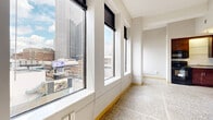Located in the heart of downtown Minneapolis on Hennepin Avenue, this efficiently designed unit offers a compelling blend of classic materials and urban convenience. Terrazzo flooring runs consistently throughout the entire space, lending a timeless, polished character to every room.

The main living area is defined by an impressive bank of large windows fitted with roller shades, flooding the space with natural light and framing panoramic views of the Minneapolis skyline, including landmarks such as Target Center and the US Bank Stadium area. A ceiling fan adds comfort to the bright, open feel of the room.

The kitchen is well-appointed with rich dark wood cabinetry, granite-style countertops, and a full suite of black appliances including a refrigerator, electric range, microwave, and dishwasher. A dedicated in-unit laundry area is tucked neatly near the entryway, providing everyday practicality.

The bathroom continues the terrazzo flooring theme and features a single-sink vanity with wood cabinetry, a full tub-shower combination, and clean, neutral finishes throughout. A closet with additional storage completes the layout.

This unit offers an ideal urban living experience, positioned within walking distance of Minneapolis's premier entertainment, dining, and cultural destinations.