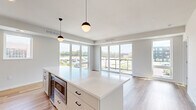 Located at 4066 Lexington Ave N in Shoreview, MN, this well-appointed 2-bedroom, 2-bathroom residence offers a thoughtfully designed single-floor layout with a clean, modern aesthetic throughout. The open-concept kitchen and living area serves as the heart of the home, featuring a large center island with white quartz countertops, white shaker-style cabinetry with matte black hardware, a herringbone tile backsplash, and stainless steel appliances including a gas range, dishwasher, and refrigerator. Globe pendant lights add a stylish touch overhead. Expansive floor-to-ceiling windows and a sliding glass door flood the living area with natural light and provide views of the surrounding neighborhood. Light hardwood flooring runs throughout the main living spaces, lending warmth and continuity. The bedrooms are carpeted for comfort, each offering generous closet storage with built-in shelving systems. The primary bedroom features its own en-suite bath with a frameless glass walk-in shower adorned with geometric tile, matte black fixtures, and wood-look flooring. A well-lit hallway with recessed lighting and crisp white walls connects the rooms with ease. A utility room and ample closet spaces throughout add practical functionality to this refined, move-in-ready residence.
