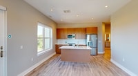 This 930-square-foot, single-floor apartment at 5118 Dexter offers a well-designed 2-bedroom, 2-bathroom layout with modern finishes throughout. The open-concept kitchen and living area serves as the heart of the unit, featuring a large center island with a quartz countertop and undermount sink, warm wood cabinetry extending to the ceiling, stainless steel appliances including a range, microwave, and refrigerator, and light hardwood flooring that flows seamlessly throughout the space. The living area opens directly onto a private balcony through glass sliding doors framed in white, offering tree-lined outdoor views. The primary bedroom measures 160 square feet and includes large windows with abundant natural light and a dedicated closet with wire shelving. The second bedroom also features generous windows with scenic views of the surrounding neighborhood. Both bathrooms are well-appointed: one showcases a dual-sink white quartz vanity with a large mirror, while the other features floor-to-ceiling travertine-style tile surrounding a soaking tub and shower combo with an illuminated mirror vanity. The unit also includes a hallway, two closets for storage, and recessed lighting throughout, creating a bright and clean modern ambiance.