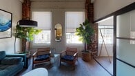Located on the seventh floor at 525 Broadway in downtown San Diego, Unit 703 Plan E is a thoughtfully designed urban residence that seamlessly merges industrial-chic architecture with contemporary living. The space is distinguished by its striking exposed brick columns, white-painted structural beams, and soaring ceilings with visible ductwork and track lighting — hallmarks of classic loft-style design.

The open-plan living and dining area forms the heart of the unit, where warm wood-look flooring flows beneath an inviting arrangement of modern furnishings. Large windows frame expansive views of the San Diego skyline, flooding the space with natural light throughout the day. The kitchen is outfitted with floor-to-ceiling cabinetry in a warm wood-grain finish, stainless steel appliances including a full-size refrigerator, dishwasher, and range, plus under-cabinet lighting that highlights the clean white countertops.

The bedroom is a serene retreat, featuring dual windows with city views, exposed brick accents, and ample room for a generous bed and additional furnishings. The bathroom is clean and contemporary, with a floating wood-toned vanity, white quartz countertop, and a well-lit mirror. Throughout the unit, the interplay of raw industrial elements and refined modern details creates a distinctive, sophisticated urban ambiance.