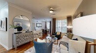 This thoughtfully designed single-floor residence offers a seamless blend of comfort and style across a well-planned layout. The open-concept living area serves as the heart of the home, featuring rich hardwood flooring, crown molding, and a ceiling fan overhead. The living room is bathed in natural light from large windows dressed with elegant drape panels and horizontal blinds, offering outdoor views. A blue accent wall adds a sophisticated touch, complemented by a glass-top coffee table and curated seating arrangements.

The kitchen is outfitted with warm wood cabinetry, black appliances, a striking marble-look countertop, a deep single-basin sink with a modern faucet, and track lighting above. It opens conveniently to a breakfast bar with acrylic seating. Adjacent to the kitchen, the dedicated dining area accommodates intimate gatherings around a round dining table, framed by natural light from a large window.

The bedrooms are carpeted for comfort, with ample natural light and thoughtful details such as built-in shelving and a reclaimed wood-framed mirror in one room. Each bedroom is served by a well-appointed bathroom featuring warm wood vanities, white countertops, and updated fixtures. A dedicated laundry room with a full-size washer and dryer and wire shelving rounds out this functional and inviting residence.