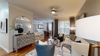 This thoughtfully designed single-floor residence offers a seamless blend of comfort and style across a well-planned layout. The open-concept living area serves as the heart of the home, featuring rich hardwood flooring, crown molding, and a ceiling fan overhead. The living room is bathed in natural light from large windows dressed with elegant drape panels and horizontal blinds, offering outdoor views. A blue accent wall adds a sophisticated touch, complemented by a glass-top coffee table and curated seating arrangements.

The kitchen is outfitted with warm wood cabinetry, black appliances, a striking marble-look countertop, a deep single-basin sink with a modern faucet, and track lighting above. It opens conveniently to a breakfast bar with acrylic seating. Adjacent to the kitchen, the dedicated dining area accommodates intimate gatherings around a round dining table, framed by natural light from a large window.

The bedrooms are carpeted for comfort, with ample natural light and thoughtful details such as built-in shelving and a reclaimed wood-framed mirror in one room. Each bedroom is served by a well-appointed bathroom featuring warm wood vanities, white countertops, and updated fixtures. A dedicated laundry room with a full-size washer and dryer and wire shelving rounds out this functional and inviting residence.