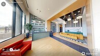 Located at 1001 Hammell Dr in Raleigh, NC, this thoughtfully designed lobby space makes a strong first impression through its bold, contemporary aesthetic. The main entrance features floor-to-ceiling glass doors framed in black steel, flooding the foyer with natural light and offering clear sightlines to the surrounding landscape. Light hardwood flooring transitions seamlessly into large-format tile, defining distinct functional zones throughout the space.

The reception area is a standout feature, distinguished by a teal tile-clad front desk set against a dramatic graphic accent wall rendered in teal and white geometric patterns. Warm wood ceiling panels and globe pendant lighting above the adjacent lounge area add depth and warmth, while a bold yellow sofa anchored by a black-and-white checkered rug creates an inviting seating zone.

A dedicated leasing or meeting office is appointed with a dark central desk, sleek white upholstered chairs, and striking vertical louvered panels that diffuse natural light from large exterior windows. Terrazzo flooring adds texture and visual interest in this area. An additional workspace features exposed concrete columns, open shelving, and generous window exposure, creating a bright and functional environment. Black steel-framed glass partitions connect the private offices to the main corridor, maintaining openness while ensuring separation. The overall ambiance balances professionalism with approachable, design-forward energy.