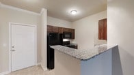 This well-appointed two-bedroom, two-bathroom residence offers a comfortable and functional layout across a single floor, complete with a private balcony that extends the living space outdoors. The kitchen is a standout feature, showcasing rich dark wood cabinetry, granite-style countertops, and a full suite of black appliances including a refrigerator, stove, and built-in microwave. A peninsula counter provides a convenient breakfast bar and adds to the open feel of the space, creating a natural connection between the kitchen and living areas. Light-toned tile flooring runs throughout, lending a clean and cohesive aesthetic that is both practical and visually appealing. Crown molding accents add a refined architectural touch to the interiors. The neutral wall palette allows for versatile décor options and enhances the sense of brightness throughout. With two full bathrooms and two generously sized bedrooms, the layout is well-suited for both everyday living and entertaining. The private balcony offers additional outdoor space, rounding out this thoughtfully designed residence.