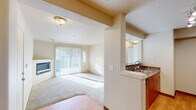 This single-floor residence offers a thoughtfully designed open layout that connects the living, dining, and kitchen areas seamlessly. The spacious living room is carpeted and bathed in natural light streaming through large sliding glass doors dressed with vertical blinds, which also provide access to an outdoor area. A built-in fireplace adds a welcoming focal point to the living space, complementing the room's warm, neutral color palette.

The kitchen is positioned adjacent to the living area and features warm-toned wood cabinetry, dark granite-style countertops, and stainless steel appliances including an electric range and over-the-range microwave. A kitchen pass-through with a sink overlooking the living area enhances the open, connected feel of the space. Wood-style flooring runs through the kitchen, contrasting with the plush carpet in the living and sleeping areas.

The bedroom is a comfortable, well-lit room with carpet flooring, a ceiling fan, a dedicated window, and a baseboard heater. The bathroom includes a wood-cabinet vanity with a dark stone-finish countertop, an undermount sink, and a large mirror with overhead lighting. Textured ceilings are consistent throughout the unit, adding a classic residential character to the overall design.