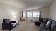 This 2-bedroom, 1-bathroom single-floor unit offers a straightforward and functional layout well-suited for everyday living. The living room is a generously sized, carpet-floored space featuring multiple windows that admit ample natural light and provide outdoor views. A dedicated dining area is accessible through an open passageway, creating a connected and practical flow between spaces. Baseboard heating is present throughout, and a wall-mounted AC unit is also featured in the living area.

The kitchen is equipped with warm-toned oak cabinetry, white appliances including a gas range and full-size refrigerator, light countertops, and tile-style flooring. A window above the sink adds natural light to the workspace.

Both bedrooms are carpeted and feature ceiling fans. One bedroom includes a window with outdoor views, while the other offers a more private setting. Each room provides a comfortable and quiet retreat.

The bathroom is finished with gray square wall tile surrounding a full soaking tub, complemented by tile-style flooring and a window with vertical blinds. The overall ambiance of the unit is clean, neutral, and move-in ready.