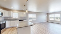 Located on 40th Ave S in Fargo, North Dakota, this well-appointed two-bedroom, two-bathroom single-floor residence offers a thoughtfully designed layout with a comfortable and modern feel throughout. The open-concept kitchen and living area serves as the heart of the home, featuring warm light wood flooring, a central granite-topped island with pendant lighting, crisp white cabinetry, granite countertops, a stainless steel appliance suite including a refrigerator, range, microwave, and dishwasher, and a window above the sink. The spacious living room extends naturally from the kitchen, bathed in natural light from a large multi-pane window with outdoor views and includes a wall-mounted air conditioning unit and baseboard heating. Both bedrooms are carpeted and offer a neutral, serene atmosphere — the primary bedroom is generously sized, while the second bedroom also benefits from natural light via a large window. The two bathrooms feature light wood-style vinyl flooring; one includes a full tub-shower combo with a curved curtain rod and an adjacent closet with open shelving. A dedicated laundry room with in-unit washer and wood-style flooring with overhead wire shelving adds everyday convenience. Throughout, the design favors clean lines, neutral tones, and practical finishes.