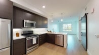 Located at 1540 Vine St in Hollywood, Los Angeles, this modern single-floor residence offers a clean, contemporary design throughout. The open-concept kitchen is a standout feature, outfitted with rich dark-toned cabinetry that extends to the ceiling, crisp white quartz countertops, a marble-style tile backsplash, and a full suite of stainless steel appliances including a gas range, built-in microwave, dishwasher, and refrigerator. Light wood flooring flows through the kitchen and living areas, complementing the bright, minimalist aesthetic. Pendant lighting over the kitchen adds a modern touch, while large windows invite abundant natural light into the living space, creating an airy and open ambiance. The bedroom features plush carpeting, a ceiling fan, and a generously sized window with views of the surrounding building exterior. A second carpeted room offers flexible use as an additional bedroom or office. The bathroom is finished with classic penny-tile flooring, a dark vanity with white countertop, and a large mirror, and connects directly to a dedicated walk-in closet. A smart home panel and keypad entry are also present, adding a layer of convenience and security to this well-designed Hollywood residence.
